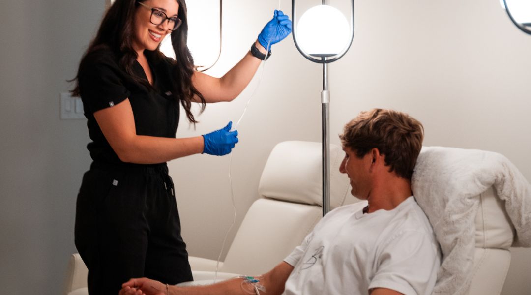 nurse in black scrubs administering intravenous vitamin therapy for young man relaxing in white recliner at relive health
