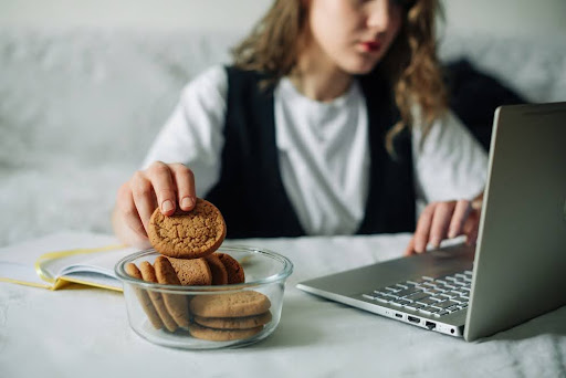 Woman eating cookies mindlessly while she works. Bad food choices can make weight loss hard