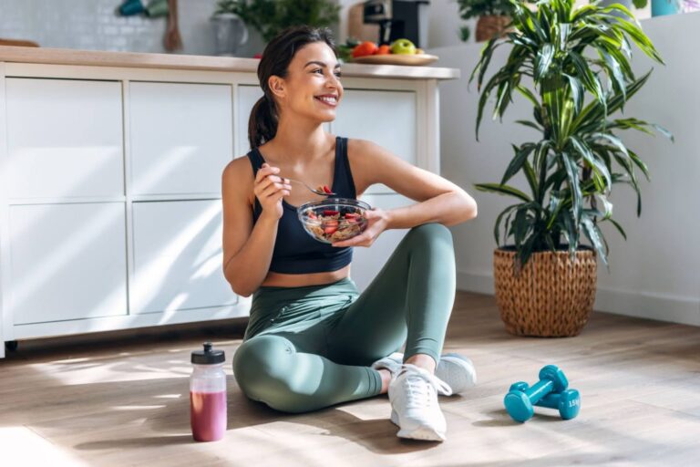 woman eating a healthy breakfast on the floor in workout clothes and dumbbells beside her