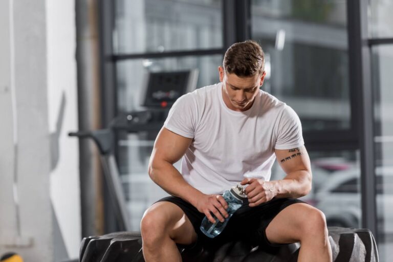 young man sitting on gym bench holding water bottle with head down