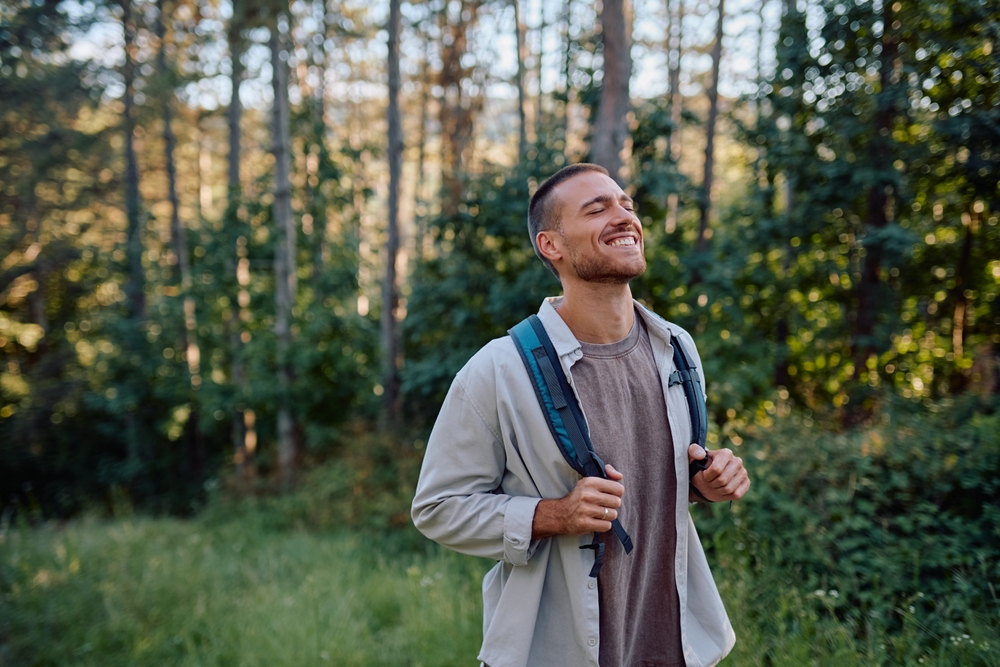 A smiling young man hiking in the woods, representing the cellular repair and mobility benefits of stem cell injections at Relive Brentwood.