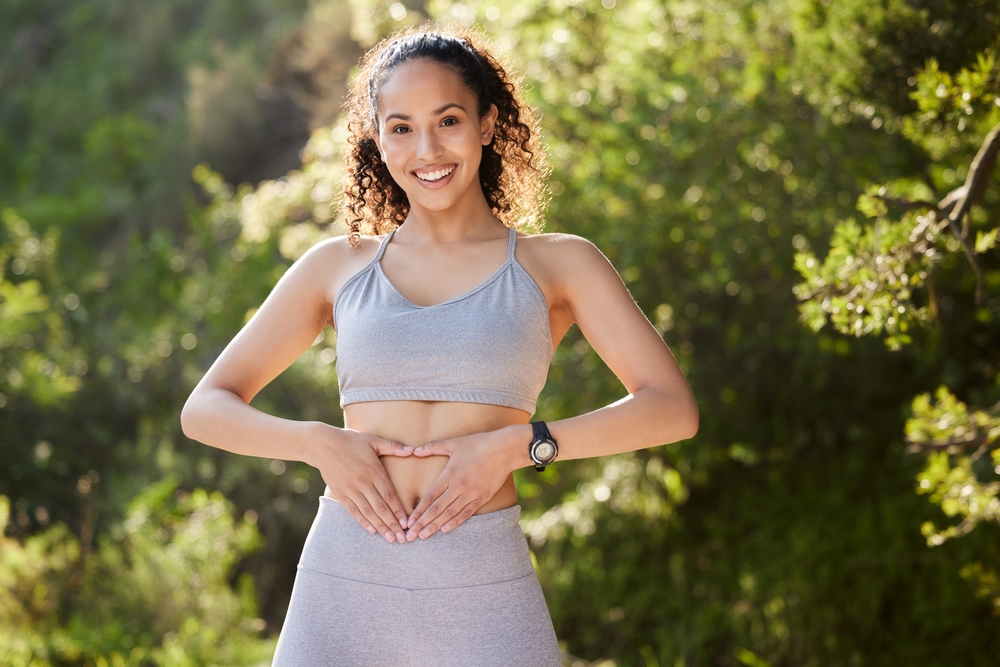 A smiling woman holding her hands over her stomach to symbolize gut health and the anti-inflammatory benefits of KPV peptide therapy at Relive Brentwood.
